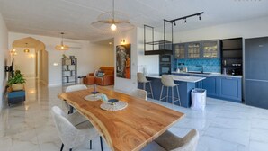 A modern kitchen with blue cabinets, a wooden dining table, and a large island. - A lovely, central 2BR penthouse with large outdoor (L-Iklin)