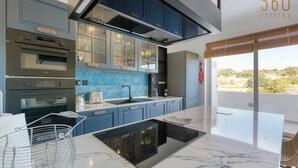 A modern kitchen with dark blue cabinets, a black countertop, and a large window overlooking a scenic landscape. - A lovely, central 2BR penthouse with large outdoor (L-Iklin)