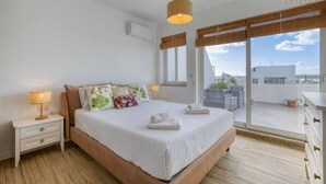 A bedroom with a large bed, bedside lamps, a window with a view, and a ceiling fan. - A lovely, central 2BR penthouse with large outdoor (L-Iklin)
