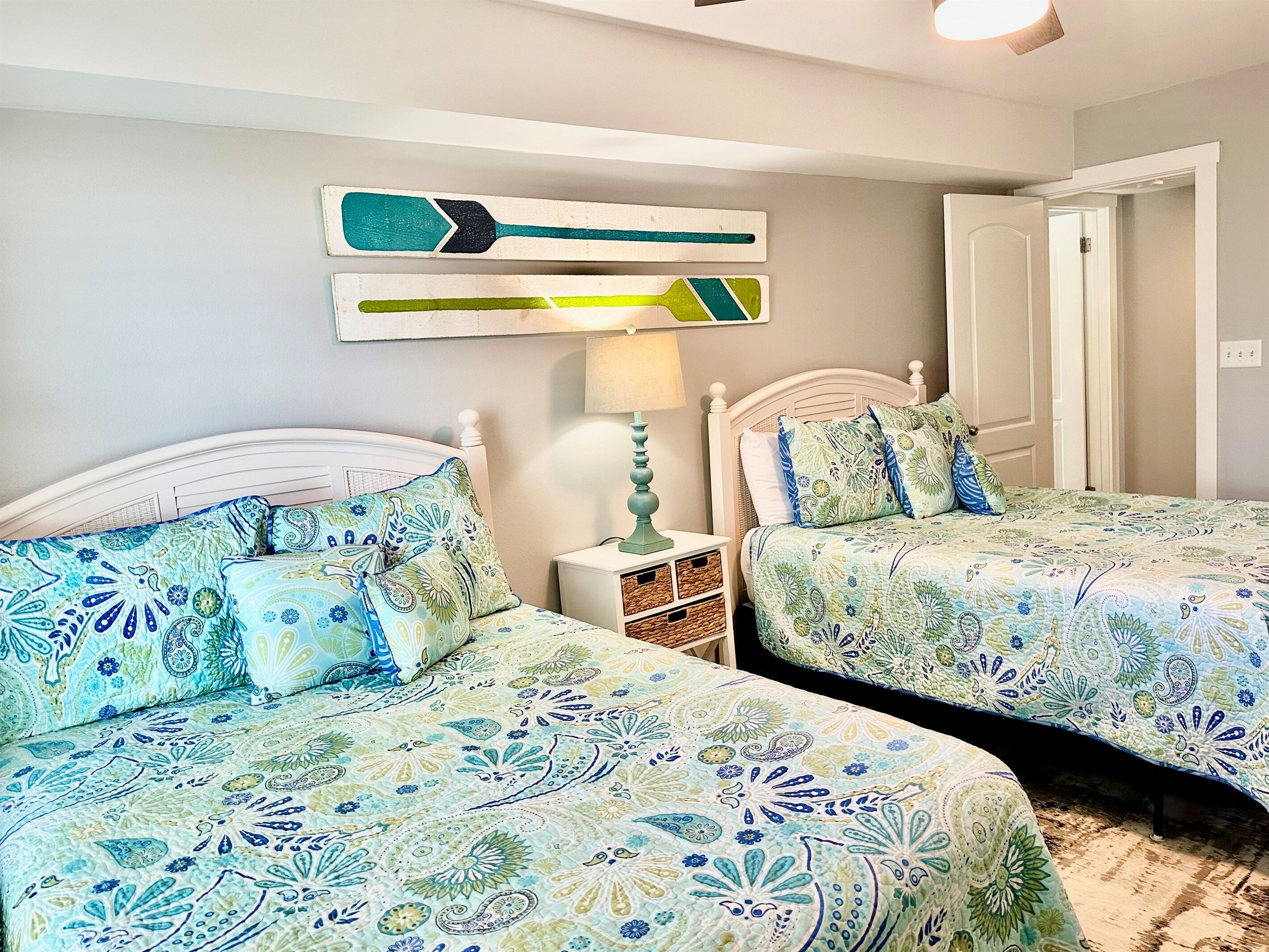 A bedroom with two beds, a nightstand, a lamp, and a wall art piece.