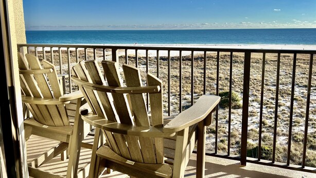 Un balcon avec deux fauteuils Adirondack donnant sur une plage.