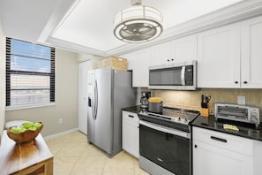 A modern kitchen with white cabinets, stainless steel appliances, and a wooden table with a bowl of apples.