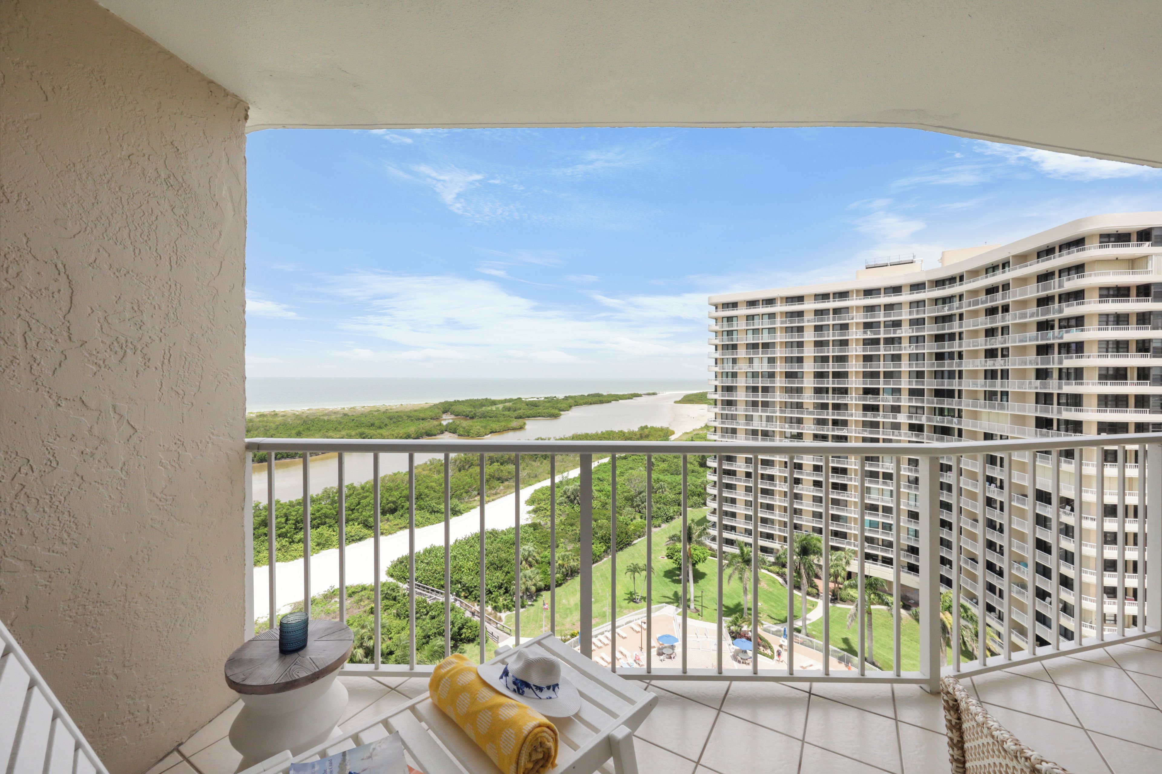 A balcony with a view of a river, greenery, and a high-rise building.