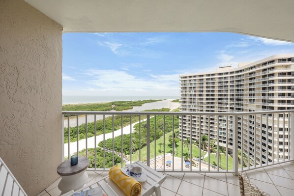 A balcony with a view of a river, greenery, and a high-rise building.