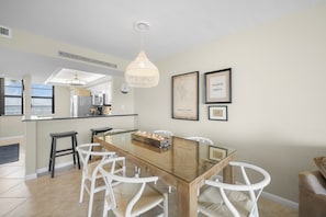 A modern kitchen with a glass dining table, white chairs, and a hanging light fixture.