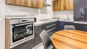 A modern kitchen with wooden cabinets, a built-in oven, and a round wooden table. - POOL access and a beautiful 1BR APT in Swieqi (Is-Swieqi)