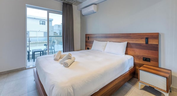 A hotel room with a large bed, a wooden headboard, a bedside table, and a view of the outside. - A fully equipped APT with private balcony & Pool (Is-Swieqi)