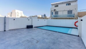 A rooftop pool with a lifebuoy, a black ottoman, and a clear sky. - A fully equipped APT with private balcony & Pool (Is-Swieqi)