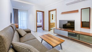 A modern living room with a sofa, a coffee table, a TV, and a dining area. - A fully equipped APT with private balcony & Pool (Is-Swieqi)