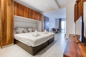 A modern hotel room with a large bed, wooden paneling, a flat-screen TV, and a dining area visible in the background. - Spacious, fully equipped 1BR maisonette with Pool (Is-Swieqi)