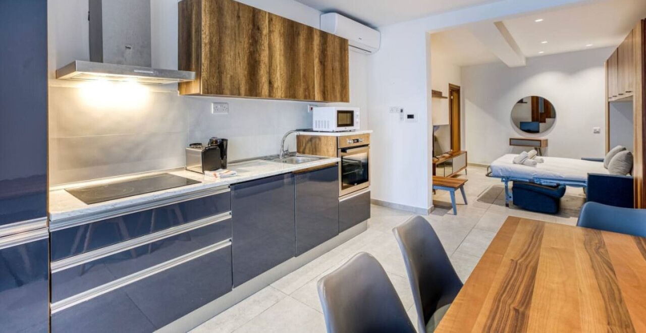 Una cocina moderna con electrodomésticos integrados, un comedor con mesa de madera y un dormitorio con cama y mesitas de noche.