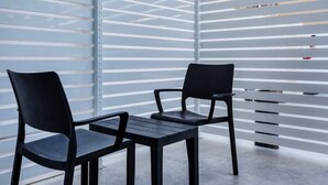 A modern outdoor seating area with two black chairs and a small table, set against a metal wall with horizontal slats. - Spacious, fully equipped 1BR maisonette with Pool (Is-Swieqi)