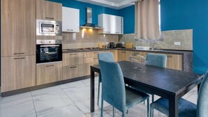 A modern kitchen with built-in appliances, a dining area with a marble table, and blue chairs. - Relaxing 2BR home with Private Balcony in Mellieha (Il-Mellieħa)