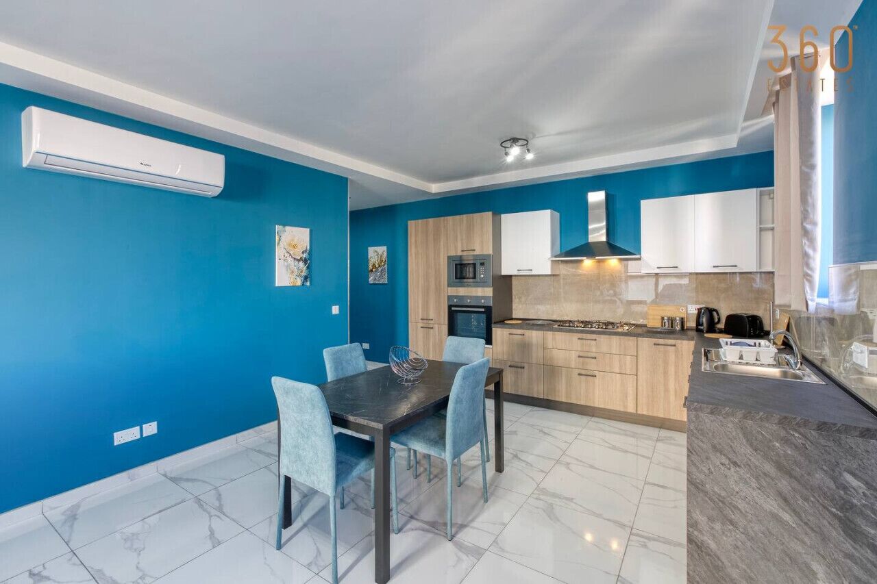 Una cucina moderna con pareti blu, un'area pranzo con tavolo e sedie e un forno integrato.