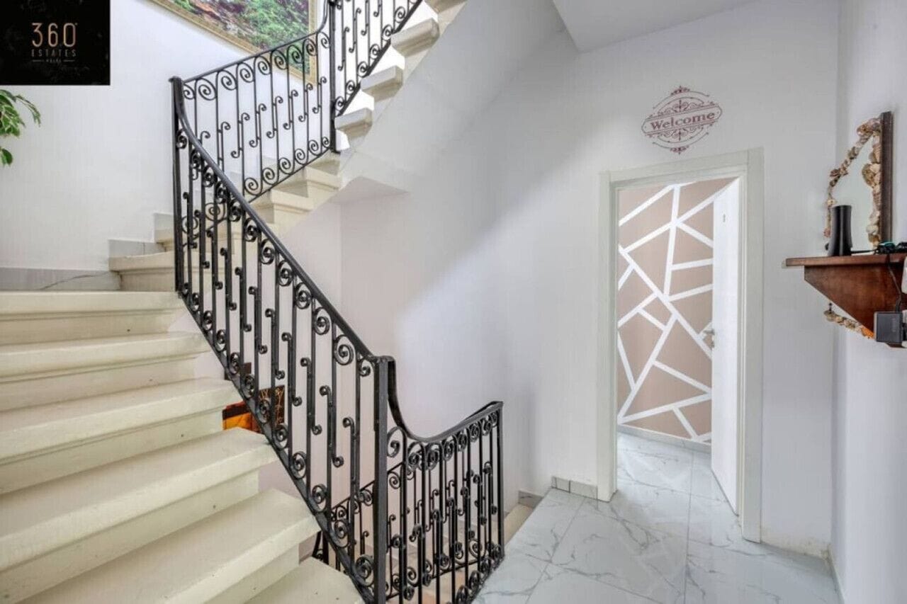 A staircase with ornate black railings leading to a door with a geometric pattern.