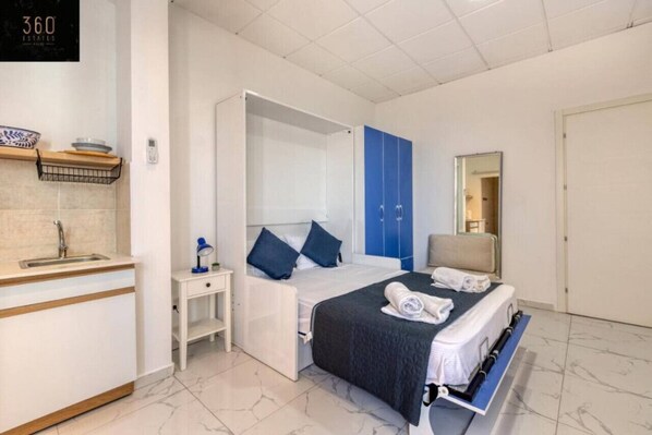 A modern hotel room with a bed, a desk, a mirror, and a wardrobe.