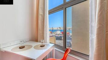 Una stanza d'angolo con una scrivania bianca, due sottobicchieri decorativi, una sedia rossa e un'ampia finestra con vista sulla città.