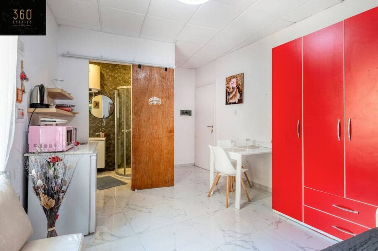 Et kompakt køkken med hvide skabe, en rød garderobe og et spiseområde med et hvidt bord og stole.