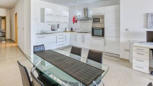 A modern kitchen with white cabinets, stainless steel appliances, and a glass dining table. - Beautiful seafront home with private balcony & BBQ (Tal-Pietà)