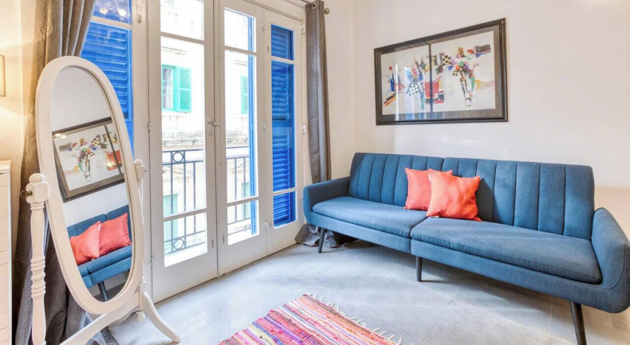 Een woonkamer met een blauwe bank, een spiegel en een kleurrijk vloerkleed.