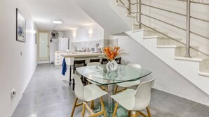A modern kitchen with white cabinets, a glass dining table, and a staircase with a metal railing. - An amazing 2BR home with a special private rooftop (Tas-Sliema)