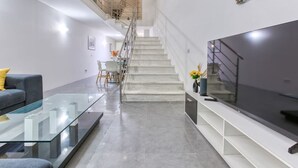 A modern living room with a glass coffee table, a sofa, a TV, and a staircase. - An amazing 2BR home with a special private rooftop (Tas-Sliema)