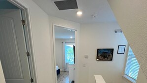 Een gang met houten vloer, witte muren en een ventilatie rooster in het plafond.