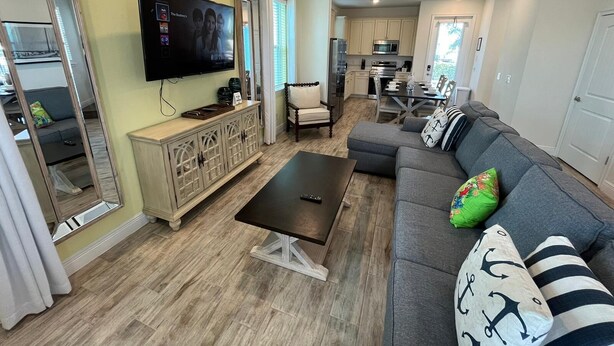 Een moderne woonkamer met een flatscreen televisie, een bank, een salontafel en een eethoek, met een keuken op de achtergrond.