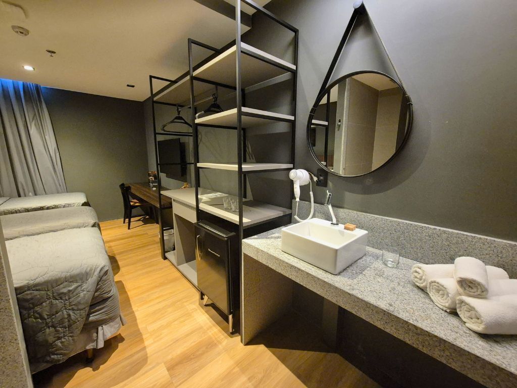 A modern hotel room with a bed, a desk, a built-in wardrobe, a sink, and a mirror.