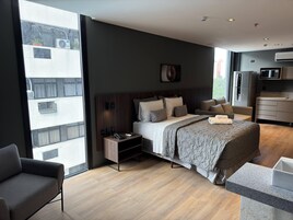 Una camera d'hotel moderna con un letto grande, comodini, un divano, angolo cottura e vista sulla città.