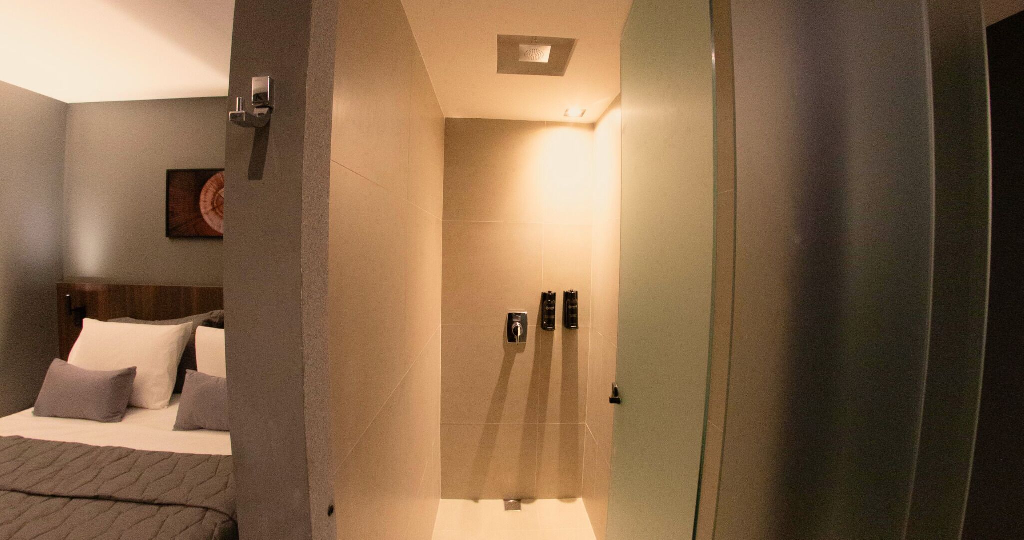 Una habitación de hotel moderna con una cama, una mesita de noche, una lámpara de pared y una puerta que da a un baño.