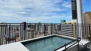 Una piscina en la azotea con barandilla de metal, rodeada de edificios altos y un cielo despejado.
