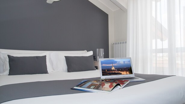 A modern hotel room with a neatly made bed, a laptop on the bed, and a magazine open. - Pepe's Home B&B (Nichelino)
