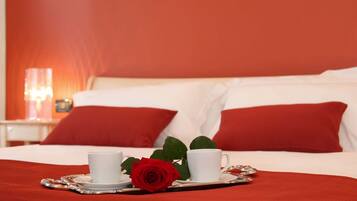 Una cama bien hecha con ropa de cama blanca y roja, dos tazas blancas sobre una bandeja y una rosa roja.