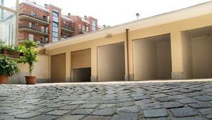 A courtyard with cobblestone pavement, a potted plant, and a building with closed shutters and balconies. - Pepe's Home B&B (Nichelino)
