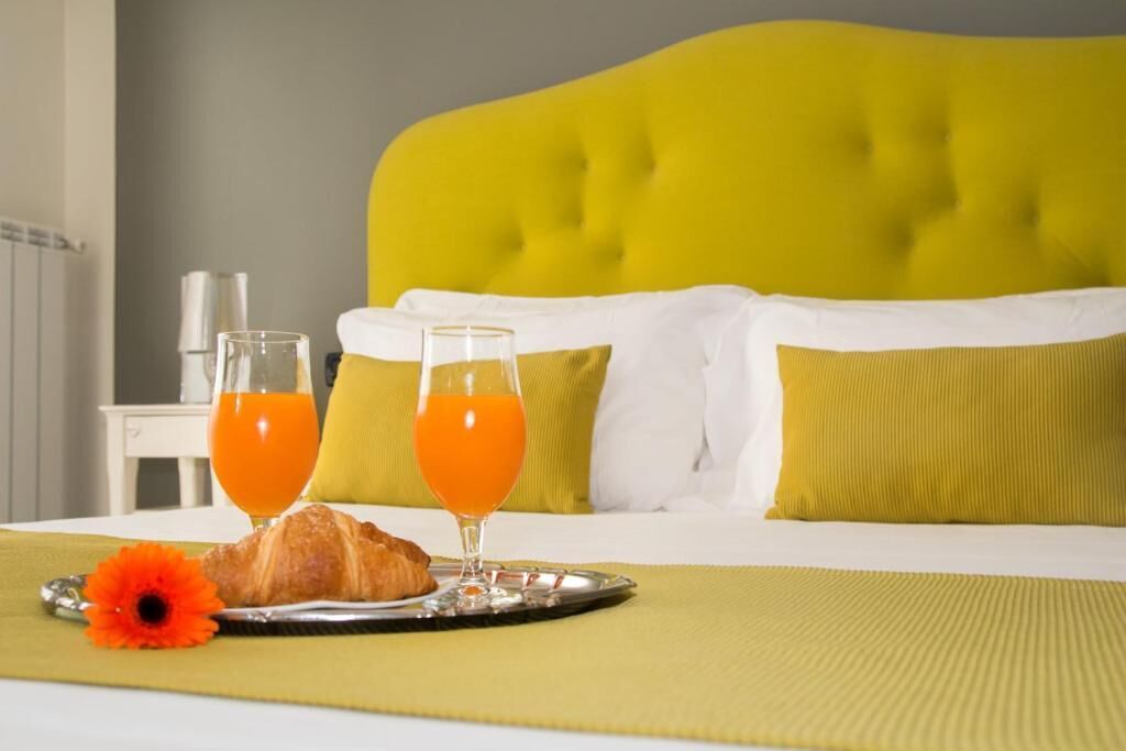 Ein Hotelzimmer mit einem Bett, einem Tablett mit Croissants und Orangensaft, sowie einer Blume auf dem Bett.
