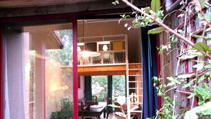 A room with a dining area, a window with a view of greenery, and a balcony with a railing.