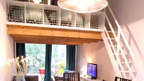 A dining area with a wooden table and chairs, a television, and a view of the outdoors through a window.
