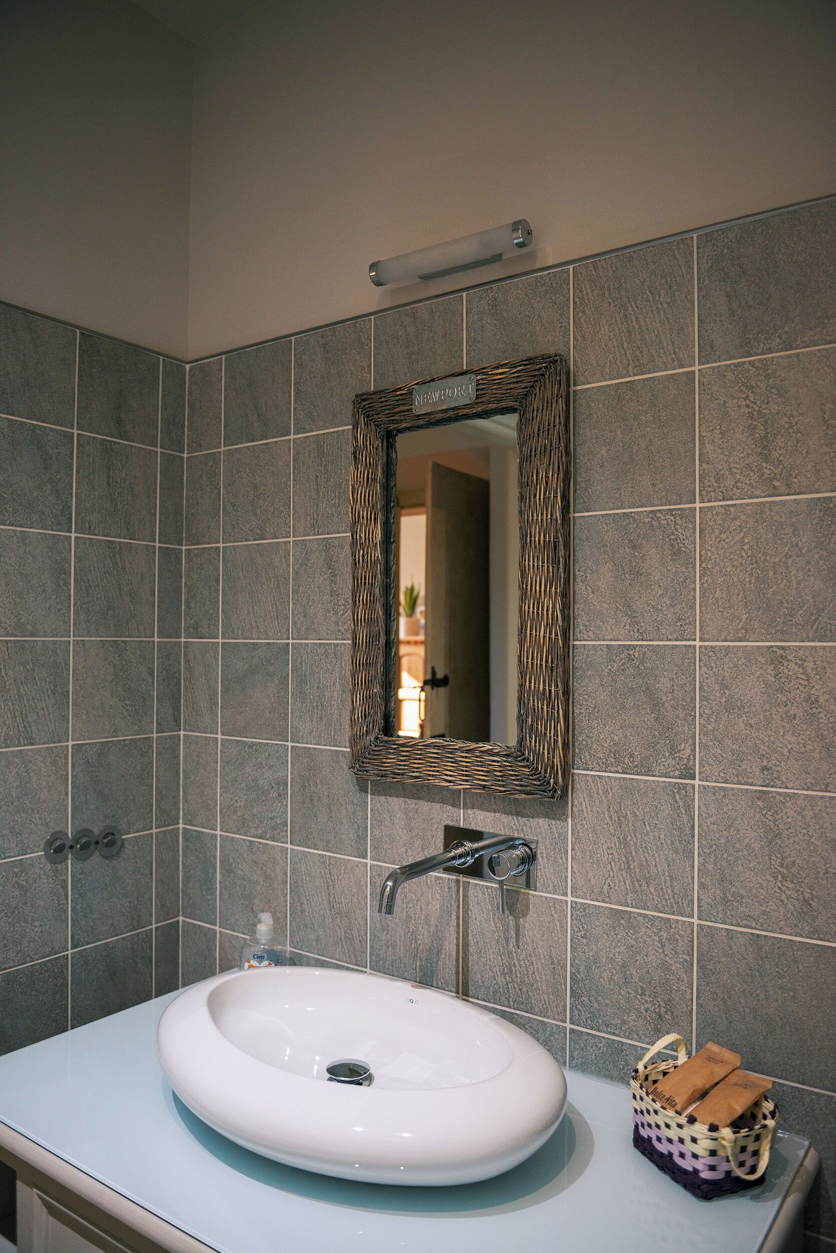 A bathroom with a white sink, a mirror with a woven frame, and a towel basket.