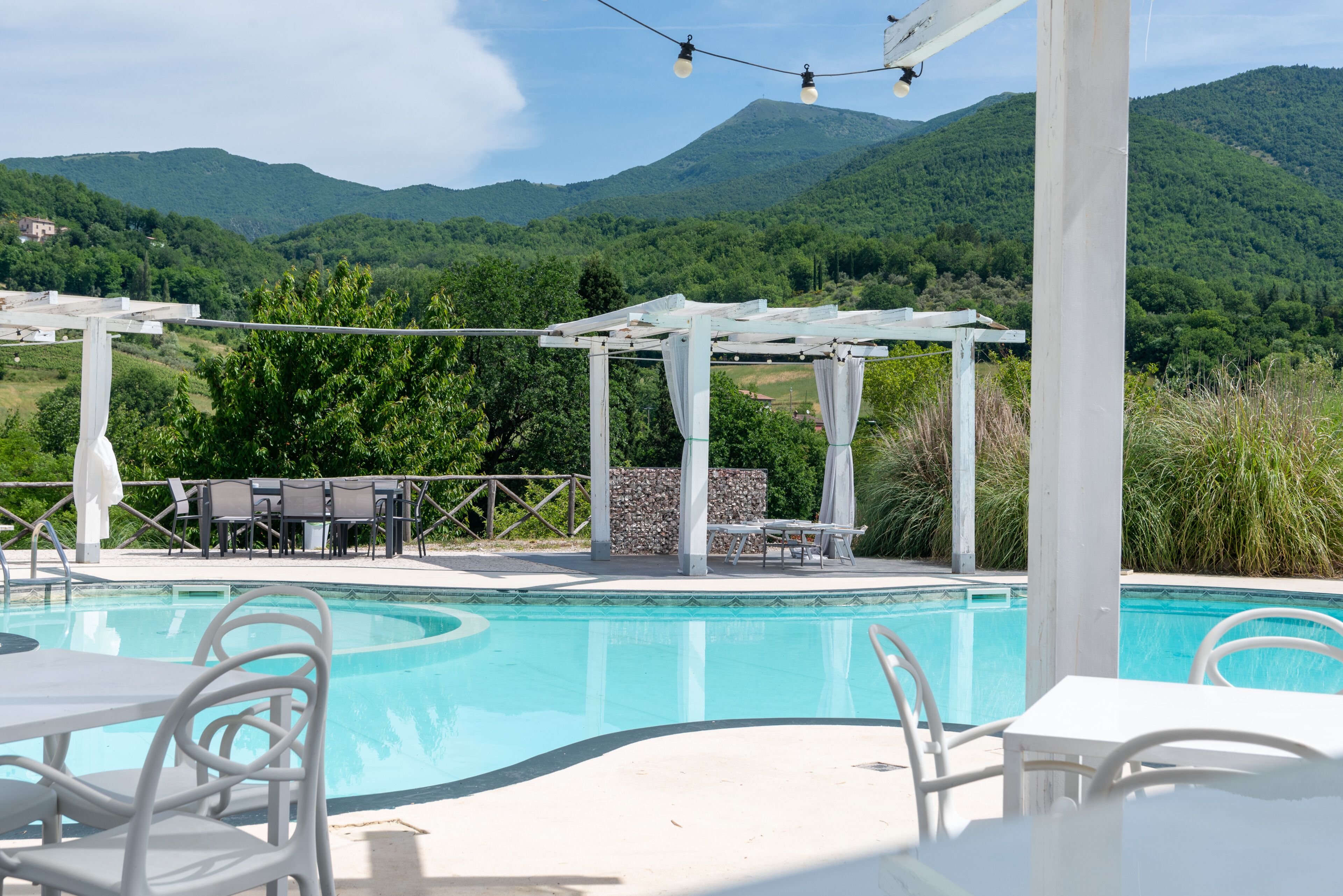 Ein Poolbereich mit Pergola, Sitzgelegenheiten im Freien und Blick auf die Berge.