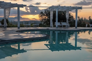 A pool area with a pergola, lounge chairs, and a view of mountains at sunset. - casa grimaldi  (Matelica)