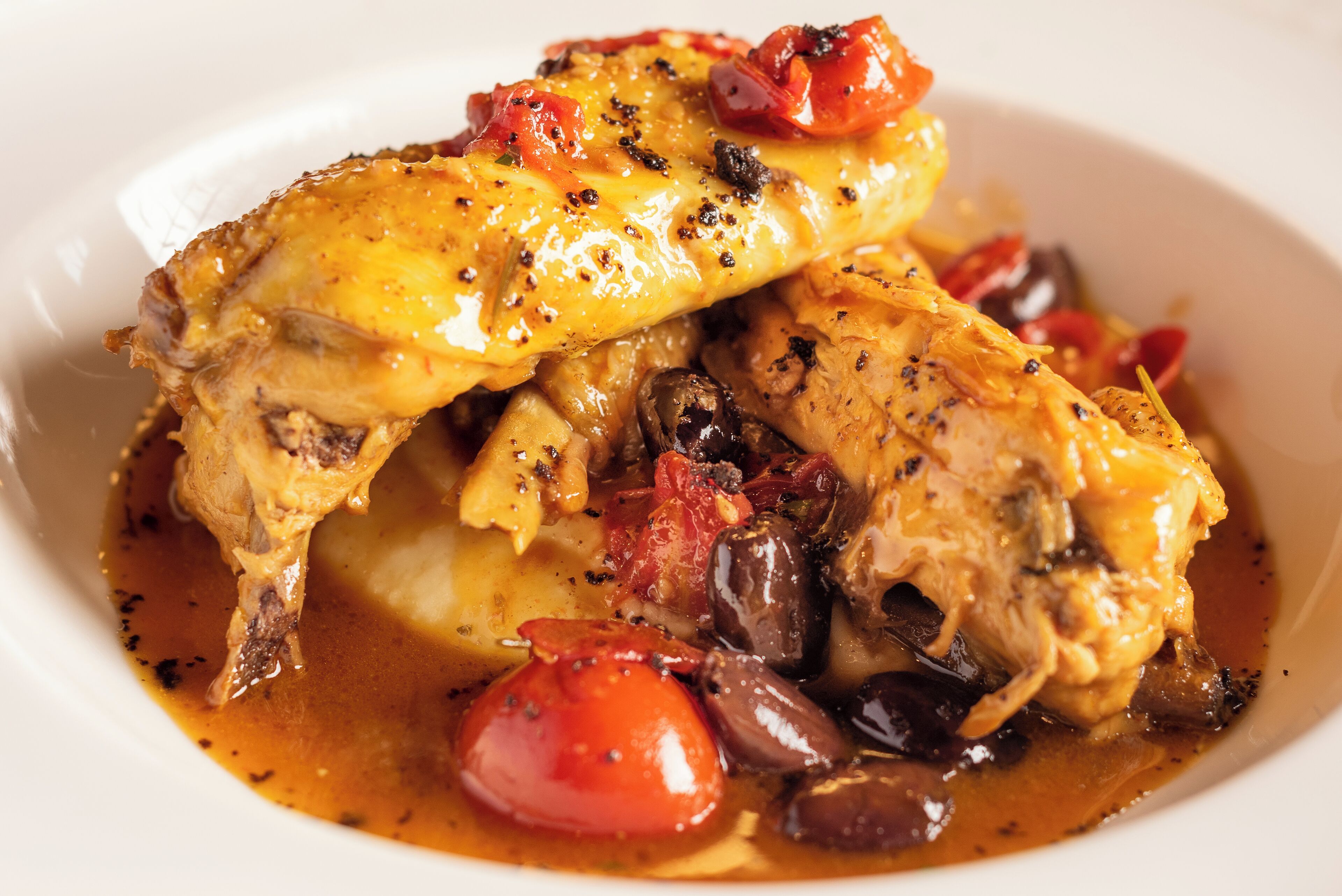 A dish with chicken, tomatoes, and olives.