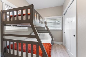 Un lit superposé avec une couverture rouge, une fenêtre avec des stores et une porte blanche.