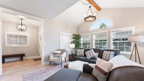 Amplia sala de estar con un sofá gris, un sillón blanco y techo de madera.