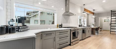 A modern kitchen with a large island, stainless steel appliances, and a view of the outside.