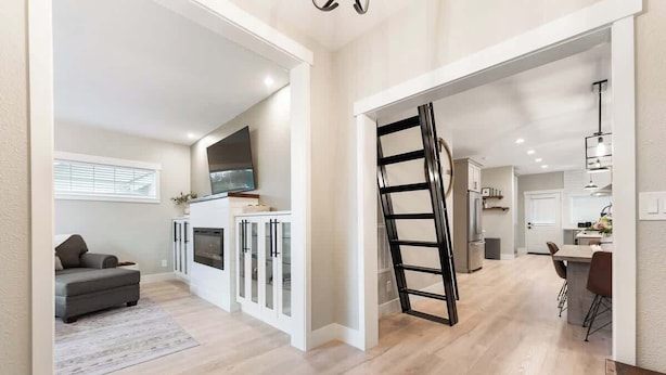 Un interior moderno con cocina, comedor y sala de estar, con pisos de madera, muebles de cocina blancos y un televisor a la vista.