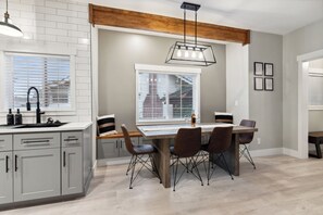 Une cuisine moderne avec des meubles de couleur grise, une table à manger en bois et un luminaire suspendu.