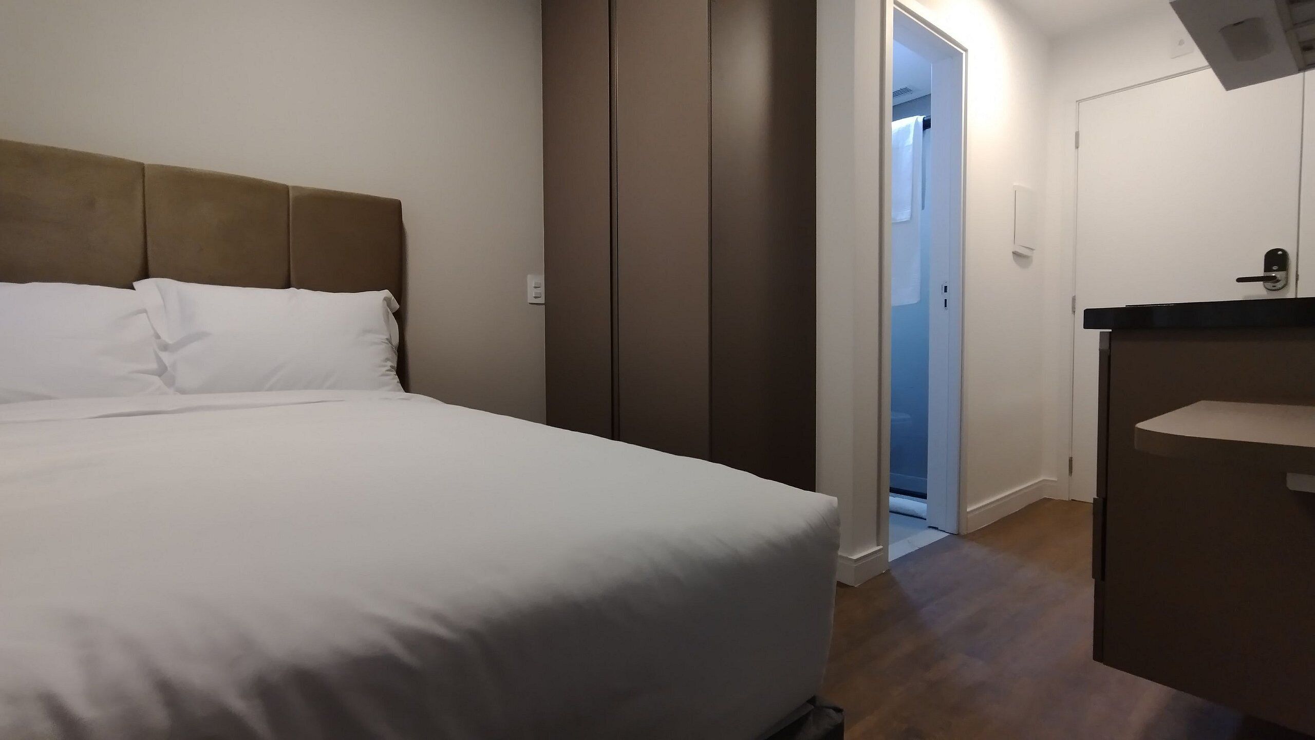 A hotel room with a bed, a wardrobe, a bathroom, and a small desk area.