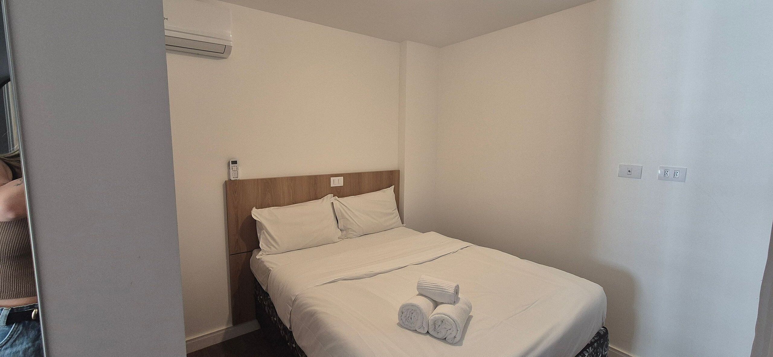 Un lit simple avec une tête de lit en bois, une literie blanche et deux serviettes enroulées posées sur le lit.