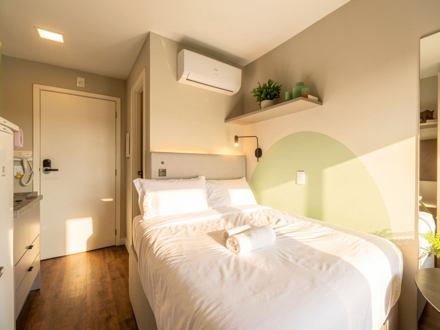 A bedroom with a bed, a bedside table, a wall-mounted air conditioner, and a shelf with decorative items.